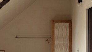 A bedroom with a sloped ceiling, a wooden bed frame, a bedside table, a hanging light fixture, and a door with a wooden frame. - Carefully renovated apartment with sea view in Saint Cado (Belz)