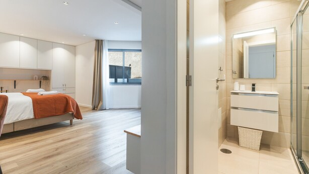 A modern hotel room with a bed, a bathroom with a mirror, and a view of the outside. - Breeze House 2 by Atlantic Holiday (Caniço)