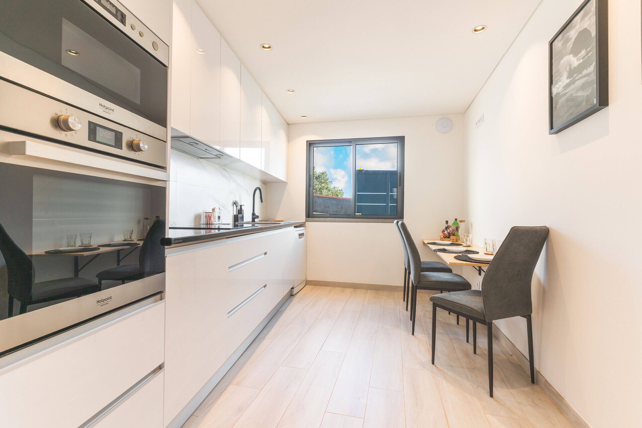 A compact kitchen with modern appliances, a dining area with a table and chairs, and a window with a view of the sky.