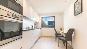 A compact kitchen with modern appliances, a dining area with a table and chairs, and a window with a view of the sky. - Breeze House 2 by Atlantic Holiday (Caniço)