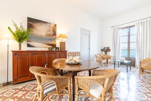A dining area with wicker furniture, a round table, and a view of the sea through large windows.