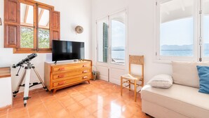 A room with a TV, wooden dresser, telescope, chair, and a sofa with a view of the sea. - Villa 'Punta Marina' with sea views, private terrace and Wi-Fi (Illes Balears)