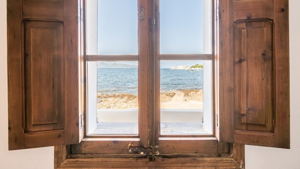 A wooden-framed window with open shutters, offering a view of a beach and distant land. - Villa 'Punta Marina' with sea views, private terrace and Wi-Fi (Illes Balears)