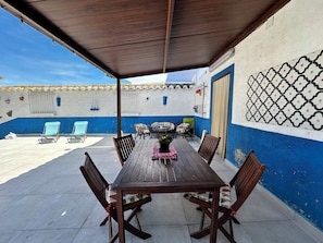 A covered patio with a wooden table and chairs, a blue and white wall with a decorative pattern, and a tiled floor.