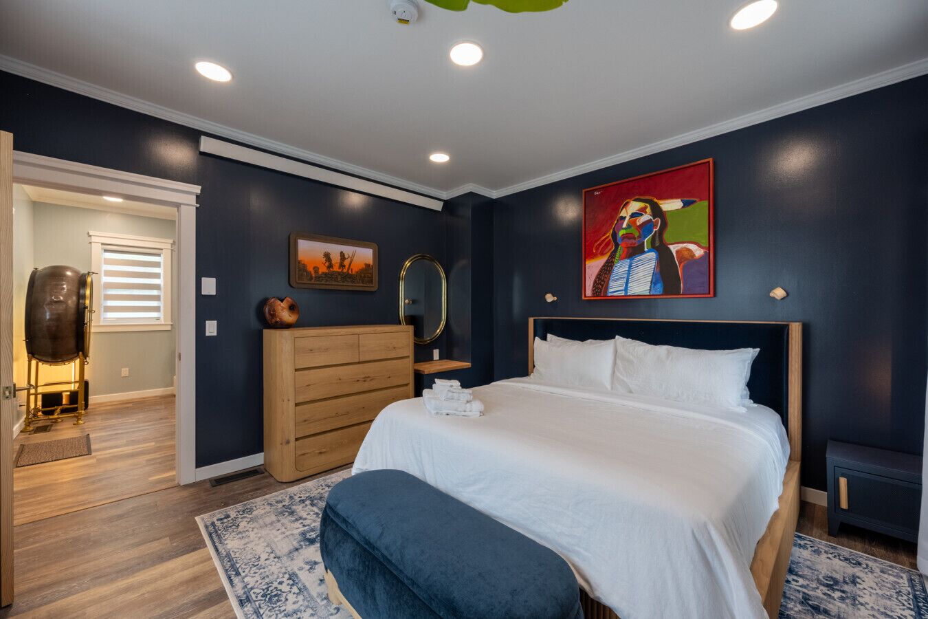 A bedroom with a bed, a dresser, a mirror, and a painting on the wall.