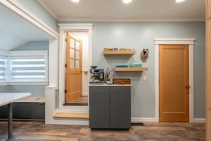 A compact kitchen with a coffee machine, shelves with dishes, and a door. - Luxury Downtown Juneau Home • Walk Everywhere • Boutique • Steps to Trails (Juneau)
