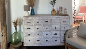 A rustic wooden dresser with multiple drawers, a green vase with dried plants, and a small lamp. - Gîte / furnished 3-bedroom house with veranda and garden - available 13/09 → 15/10 (Lagor)