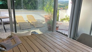 A wooden table with a cushion, a metal tray, and a wicker chair. - Gîte / furnished 3-bedroom house with veranda and garden - available 13/09 → 15/10 (Lagor)