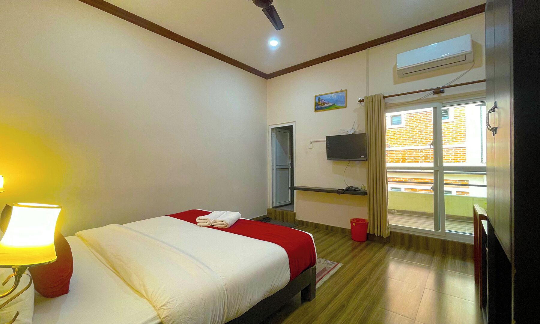 Une chambre d’hôtel équipée d’un lit, d’une télévision, d’une fenêtre donnant sur des immeubles et d’un appareil de climatisation.