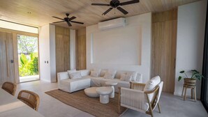 Un salon moderne avec un canapé d’angle, des tables basses rondes et un coin repas comprenant une table et des chaises.