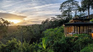 A modern villa with a wooden deck and a hammock, surrounded by lush greenery and a view of the sunset. - Chic 1BR Escape Breathtaking Balcony Views (Puntarenas)