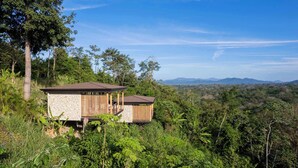 A secluded cabin with a stone facade and wooden accents, surrounded by dense forest and overlooking a mountainous landscape. - Chic 1BR Escape Breathtaking Balcony Views (Puntarenas)