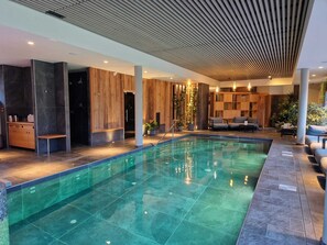 A modern indoor pool area with a clear pool, wooden panel walls, and a seating area with sofas. - Hôtel Interlaken Lounge Bar & SPA (Xonrupt-Longemer)