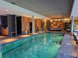 Un área de piscina interior moderna con una piscina cristalina, paredes de paneles de madera y una zona de estar con sofás.