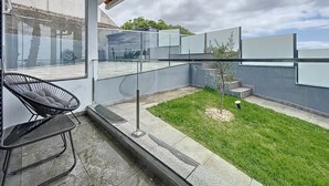 A modern outdoor balcony with a glass railing, a small lawn, and a chair. - Breeze House 2 by Atlantic Holiday (Santa Cruz)