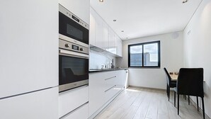 A modern kitchen with white cabinetry, a built-in oven, and a dining area with a table and chairs. - Breeze House 2 by Atlantic Holiday (Santa Cruz)