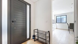 A modern interior with a dark wooden door, a glass shelf, and a view of a kitchen and balcony. - Breeze House 2 by Atlantic Holiday (Santa Cruz)