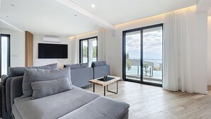 Een moderne woonkamer met een grijze bank, een flatscreen televisie en een balkon met uitzicht op zee.