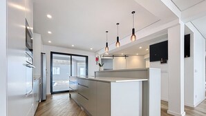 Een moderne keuken met een centraal eiland, roestvrijstalen apparatuur, hanglampen en uitzicht op het buitenland.