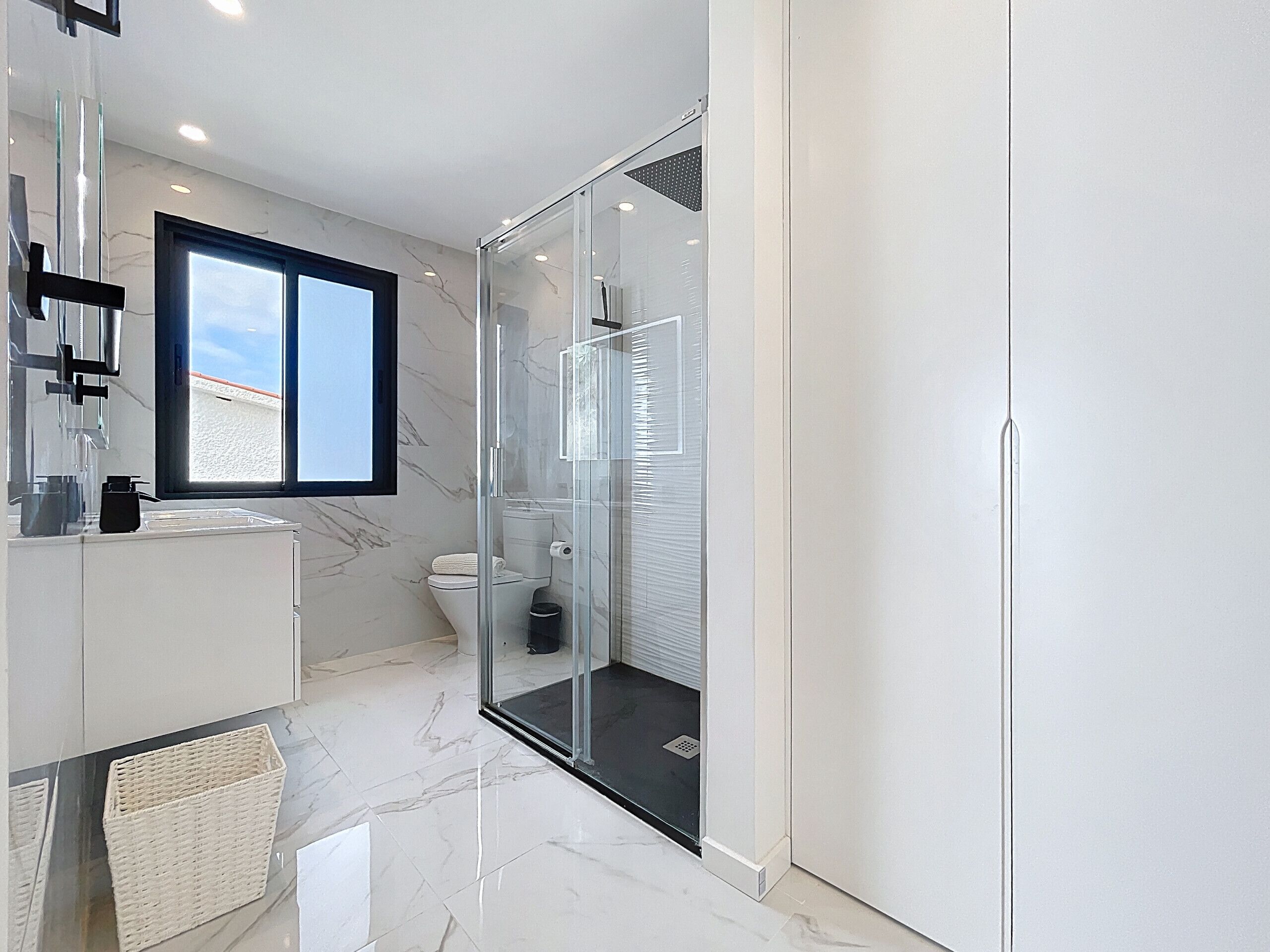 Een moderne badkamer met een glazen douchecabine, een wit toilet en een groot raam voor natuurlijk licht.