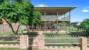 A two-story house with a balcony, a fenced yard, and a tree.