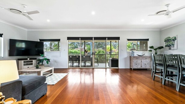 A spacious living room with a flat-screen TV, a grey sofa, wooden flooring, and a dining area with a table and chairs.