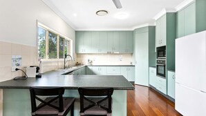 A modern kitchen with light green cabinets, a large island with two bar stools, a built-in oven, and a window with a view of boats.
