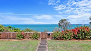 A backyard with a wooden fence, a concrete pathway, and a view of the ocean with boats. - Welcome to Cockatoos View (Point Vernon)