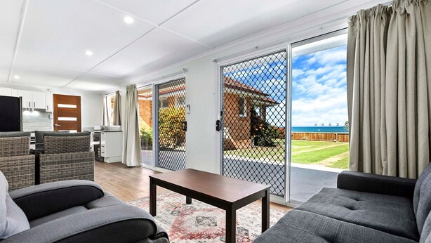 A modern living room with grey sofas, a wooden coffee table, and a kitchen in the background. - Welcome to Cockatoos View (Point Vernon)