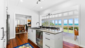 A modern kitchen with a central island, a dining area with a view, and a large window overlooking the ocean. - Extended Family Escape (Point Vernon)