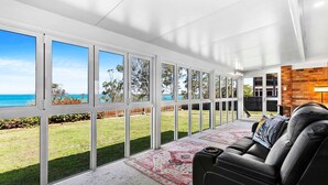 A modern living room with a large glass wall overlooking a garden and the sea. - Extended Family Escape (Point Vernon)