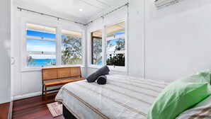 A bedroom with a bed, a bench, and large windows offering a view of the sea. - Extended Family Escape (Point Vernon)