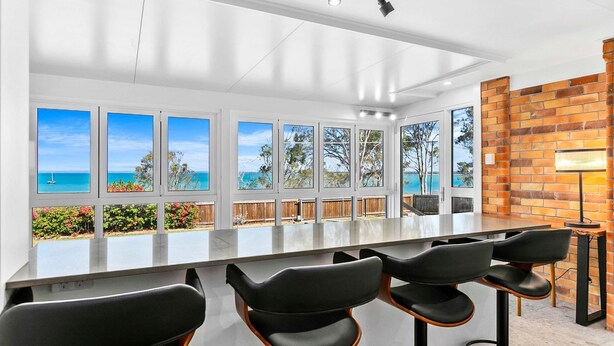 A modern kitchen with a large island, bar stools, and a view of the ocean through multiple windows. - Extended Family Escape (Point Vernon)