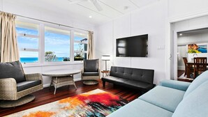 A living room with a view of the ocean, a flat-screen TV, and a dining area. - Welcome to K' Gari Dreaming (Point Vernon)