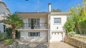 Ein zweistöckiges Haus mit einer Naturstein-Fassade, einem Balkon und einer Garage.