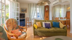 Ein Wohnzimmer mit einer Couch, Sesseln, einem Fernseher und einem Essbereich.