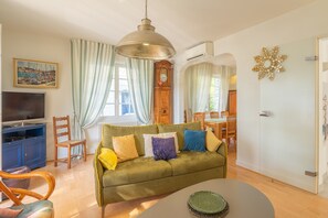 Ein Wohnzimmer mit einem grünen Sofa, Holzstühlen, einem Fernseher und einem Essbereich mit Tisch und Stühlen.