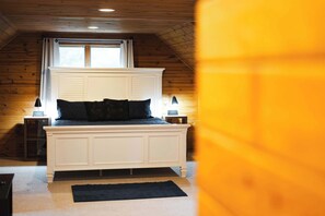 Een slaapkamer met een wit bed, donkere beddengoed, een raam met gordijnen en een houten plafond.