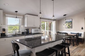 A modern kitchen with a large island, white cabinets, and a dining area with a bench and chairs. - Riverview Retreat - Pool, Hot Tub, and Mtn Views! (Harpers Ferry)