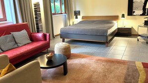 A modern bedroom with a bed, a red sofa, a small round table with a bowl, and a view of greenery through the window. - Currently not available via Fewo direkt (Söll)