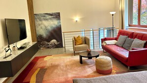 A modern living room with a flat-screen TV, a red sofa, a beige armchair, a coffee table, and a large abstract painting. - Currently not available via Fewo direkt (Söll)