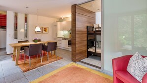 A modern kitchen with wooden cabinets, a dining area with a table and chairs, and a red sofa with a patterned pillow. - Currently not available via Fewo direkt (Söll)