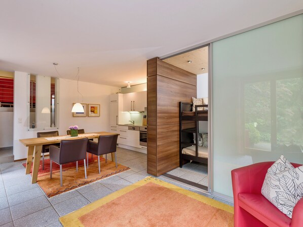A modern kitchen with wooden cabinets, a dining area with a table and chairs, and a red sofa with a patterned pillow. - Currently not available via Fewo direkt (Söll)