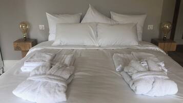 Un lit bien fait, avec du linge de lit blanc et des oreillers, deux tables de chevet avec des lampes, et des serviettes pliées posées sur le lit.