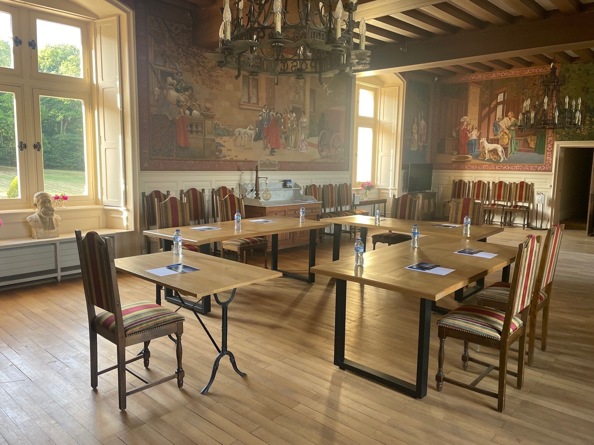 Une salle de conférence avec de longues tables, des chaises et une grande fresque murale.