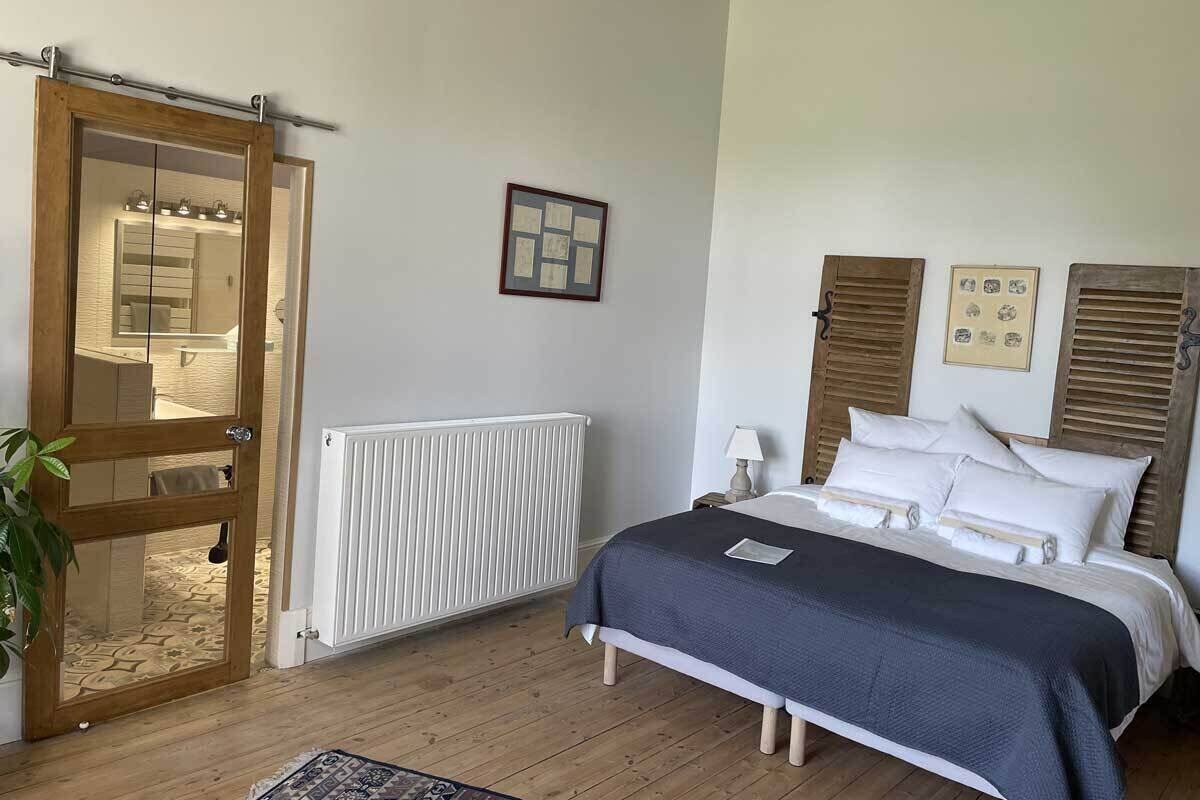 A bedroom with a wooden door, a radiator, a bed with white bedding, and a framed picture on the wall.