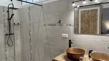 A modern bathroom with a glass-enclosed shower, a wooden vanity with copper sinks, and a mirror with a wooden frame.