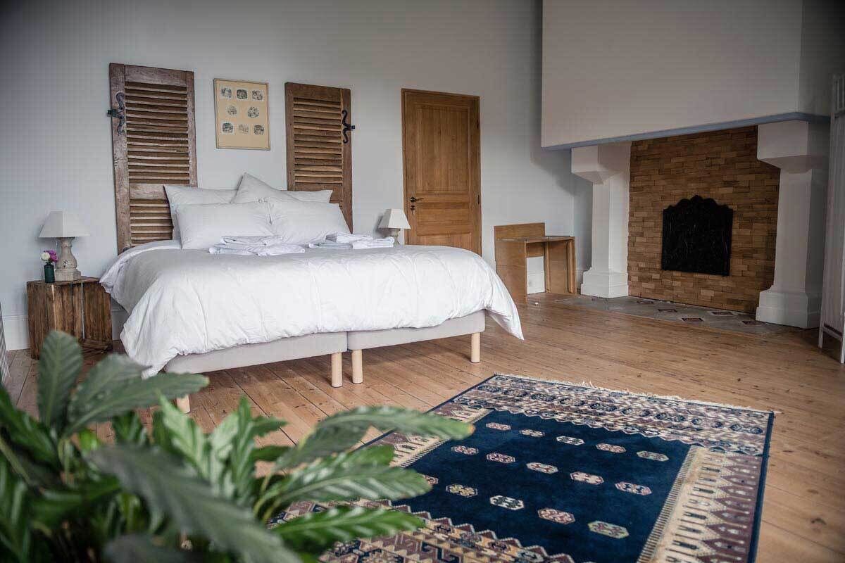 Une chambre avec un grand lit, des volets en bois, une cheminée et un tapis à motifs.