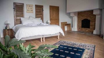 Une chambre avec un grand lit, des volets en bois, une cheminée et un tapis à motifs.