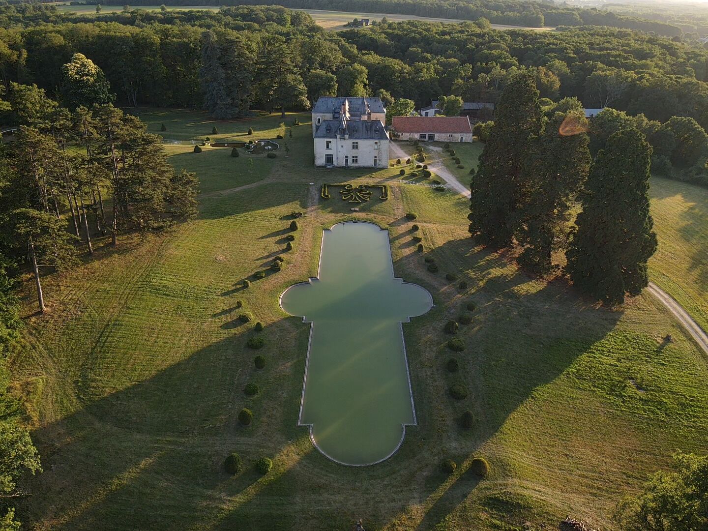 An aerial view of a large estate with a central pond, surrounded by manicured lawns and trees.
